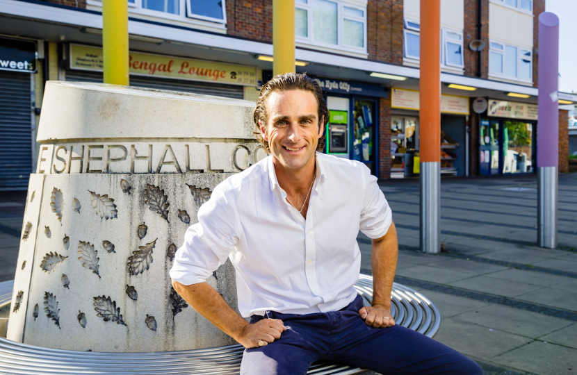 Alex sat at the Hyde Shops. Behind him is a concrete sculpture engraved with 'Shehall' as well as several different coloured pencil statutes