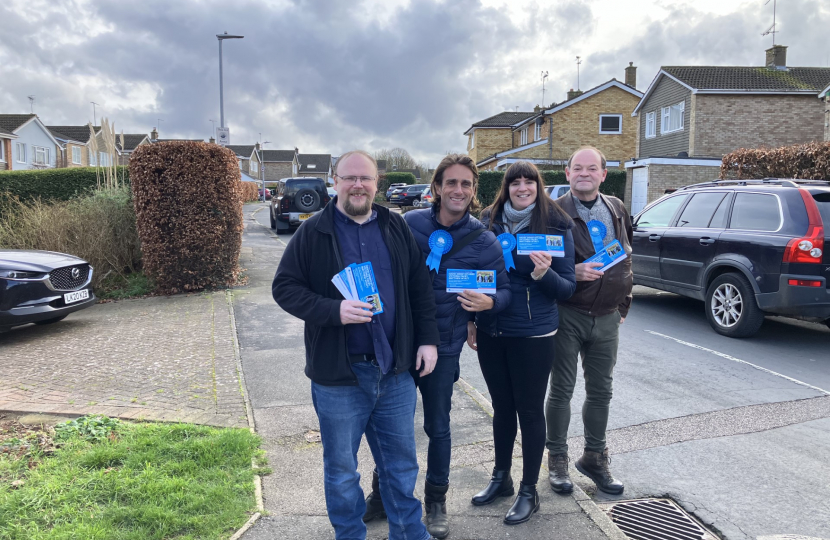 Alex Clarkson out campaigning with the Bandley Hill & Poplars Conservative team. In the background are houses, a road and a few parked cars.