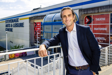 Alex Clarkson dressed smartly and smiling at the camera. Stevenage Leisure Centre is in the background.