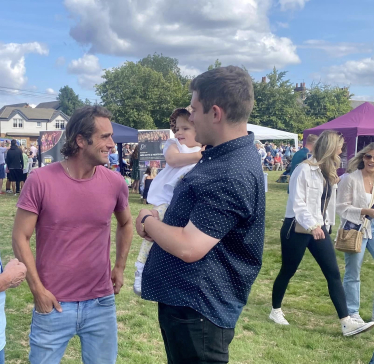 Alex Clarkson talking with a young parent at a village fete