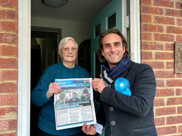 Alex Clarkson meeting with an elderly resident on their doorstep, they are both holding up one of Alex's leaflet