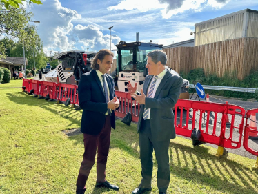 Alex talking with a Minister from the Department for Transport. They are stood in front of some building works and a tarmacking machine.